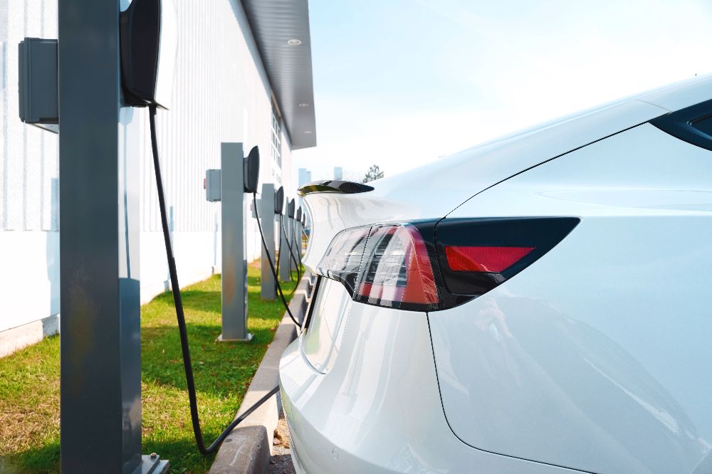  Electric cars in a row and recharging at supercharger charging stations in parking lot. EV green energy transportation background 